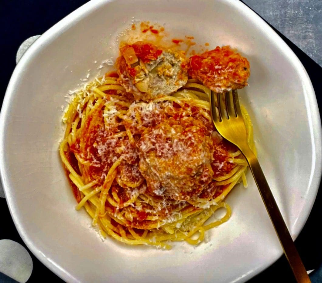 A white plate with spaghetti and meatballs on it.