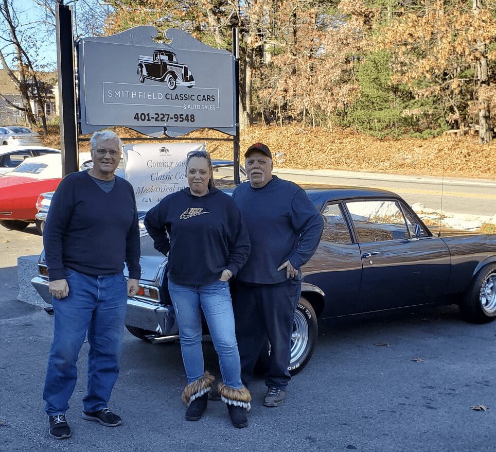 Three people standing in front of a classic car.