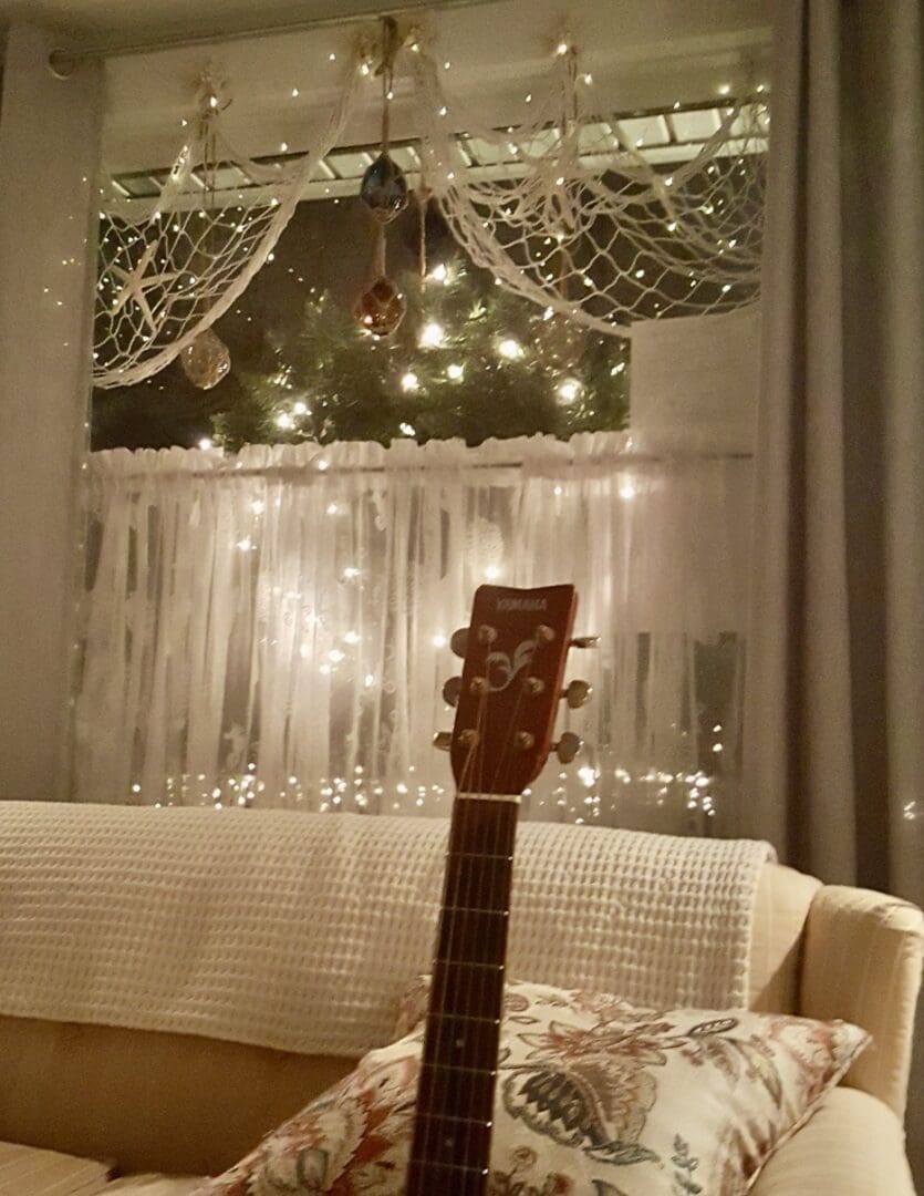 A guitar sitting on a couch in front of a window.