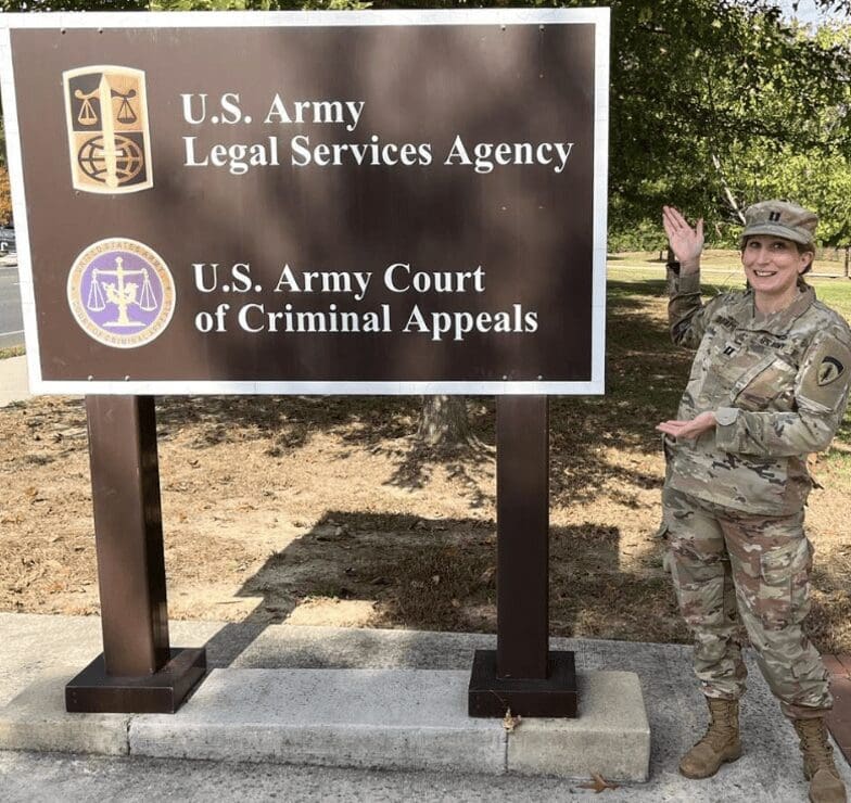 A woman in uniform standing in front of a sign that says u s army legal agency.