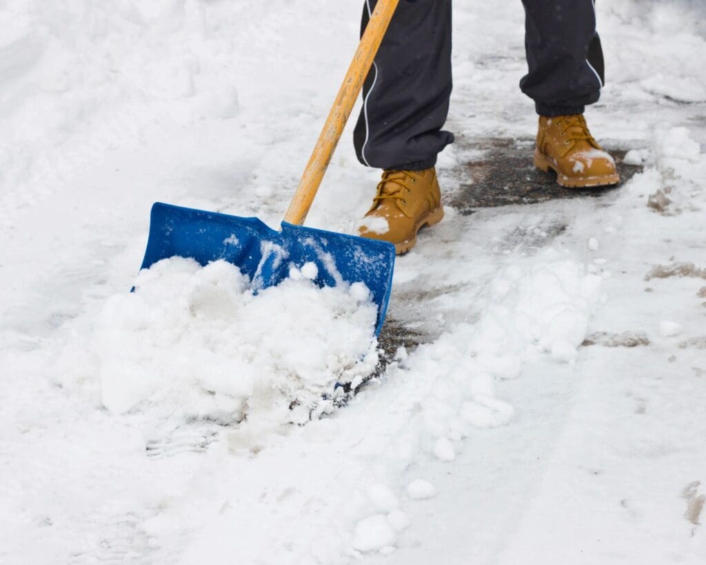 A man shoveling snow with a blue shovel.
