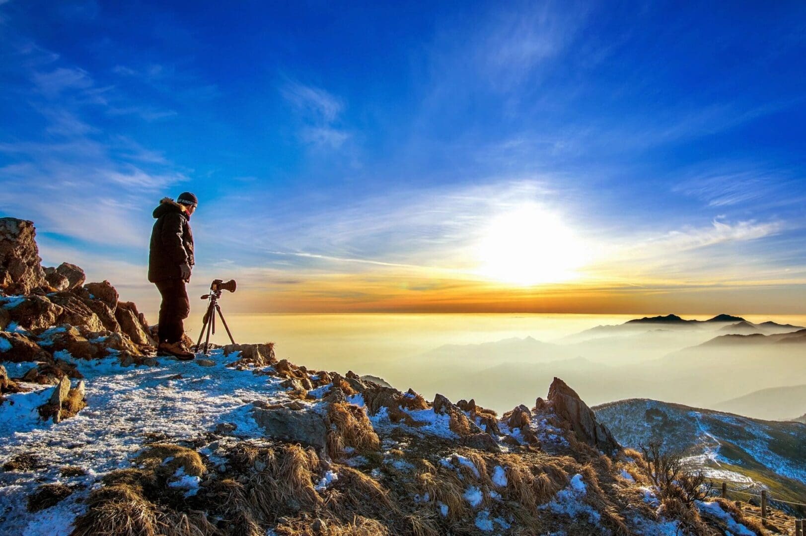 A man standing on top of a mountain with a tripod.