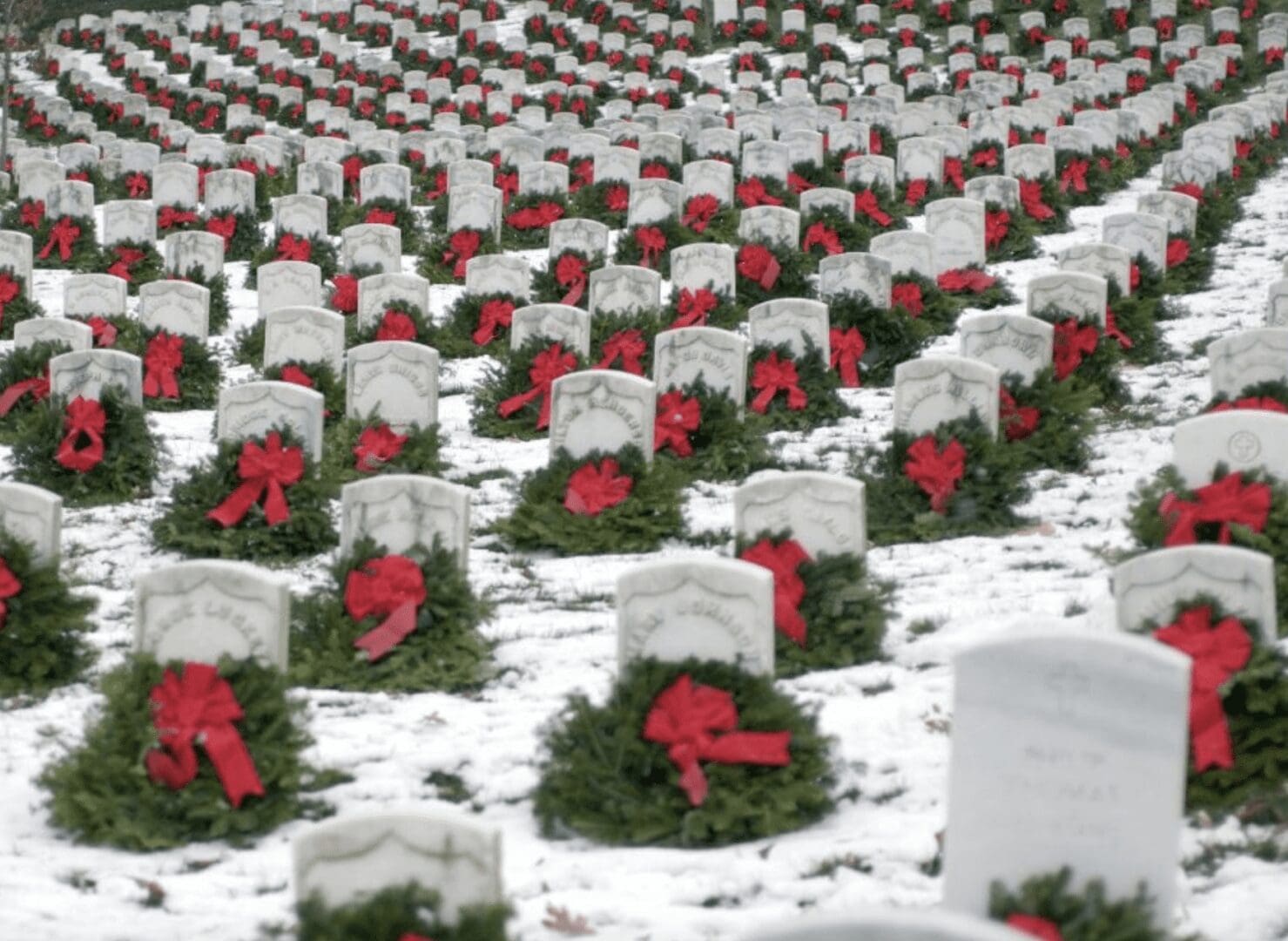 A group of headstones with red bows in the snow.