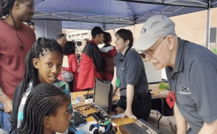 A group of children are looking at a computer at an outdoor event.