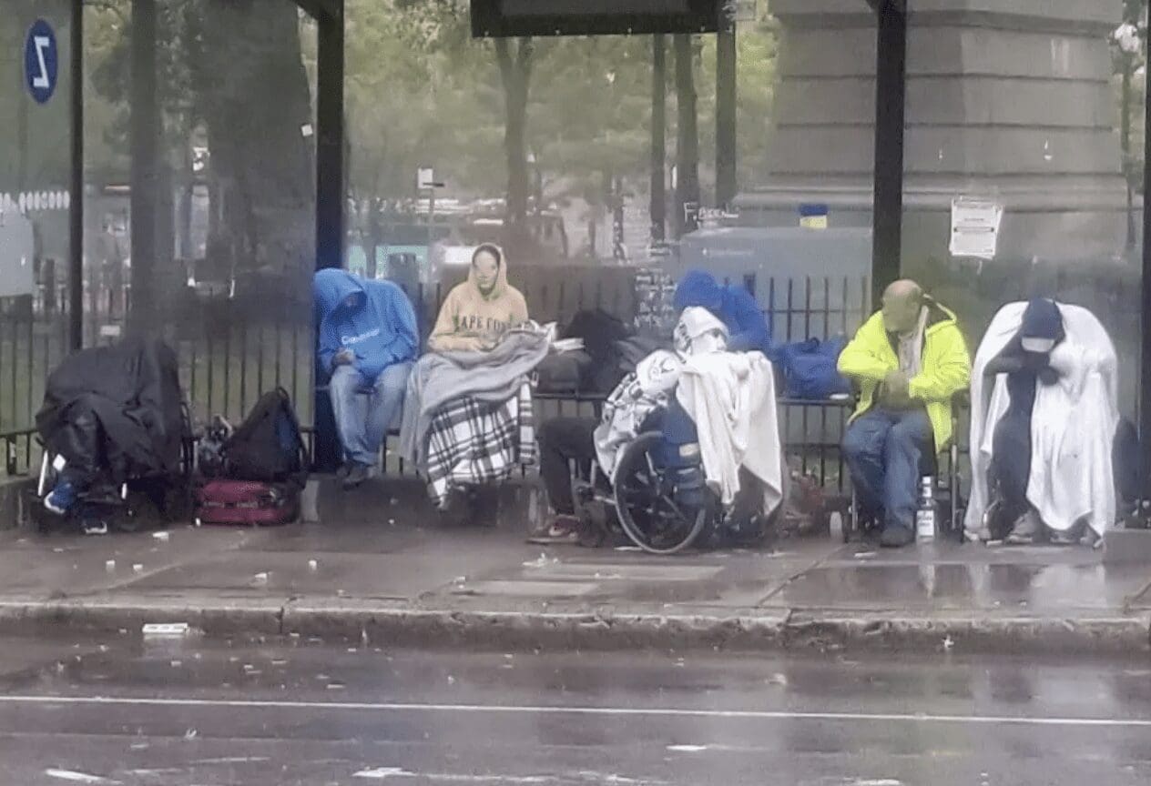 A group of people sitting on a bench in the rain.