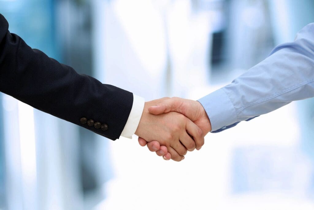 Two businessmen shaking hands in front of a blurred background.