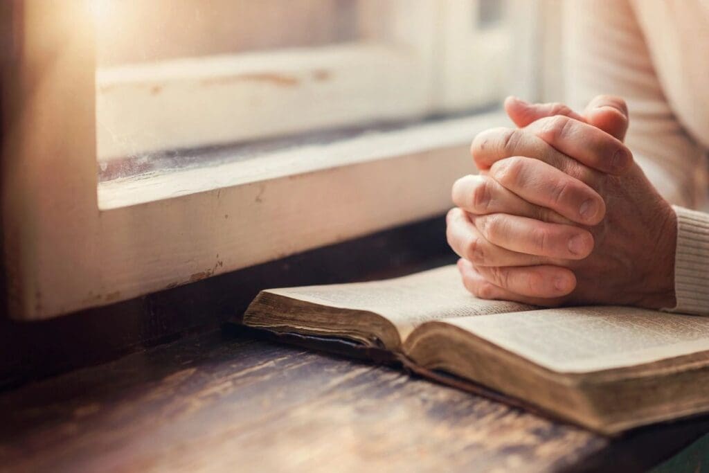 A woman praying with her hands on a bible.