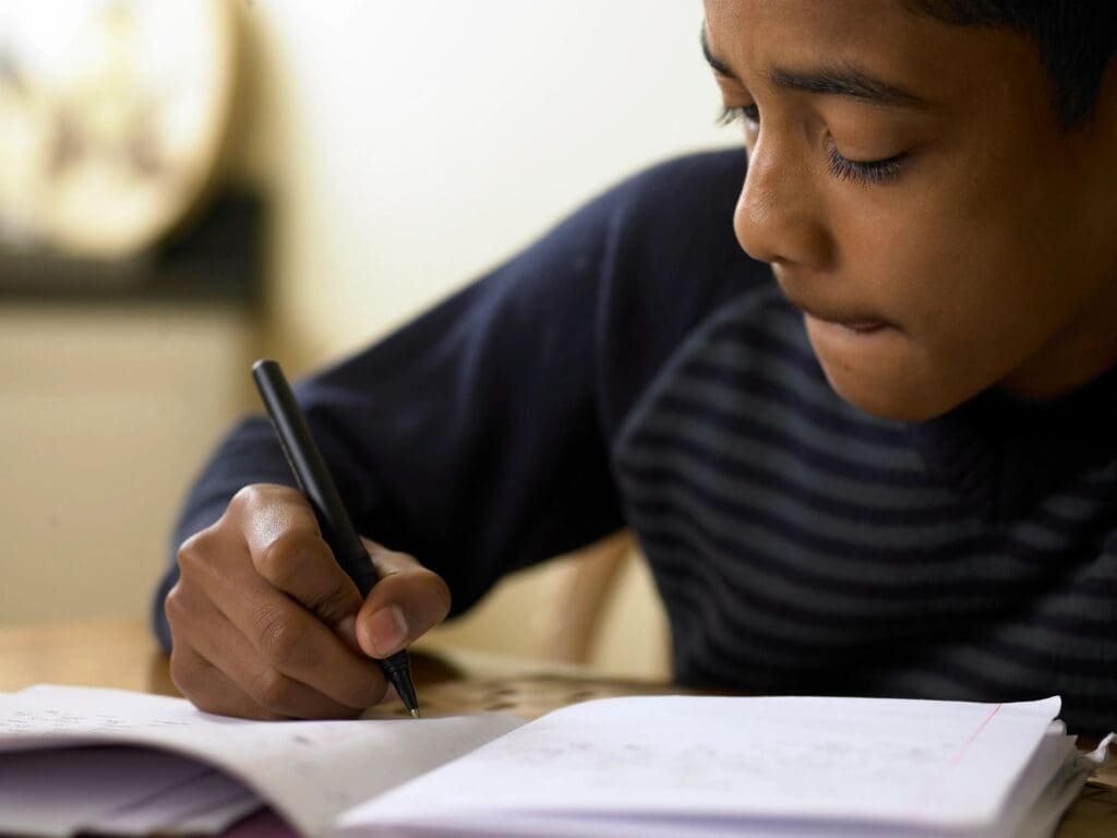 A boy writing in a notebook with a pen.