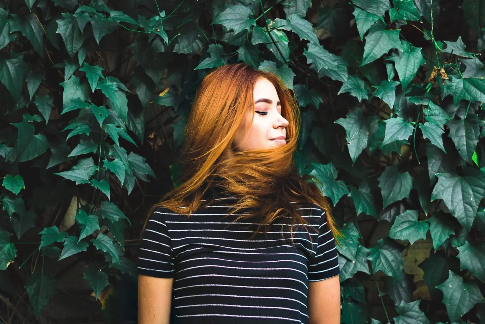 A woman with red hair standing in front of ivy.