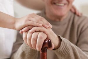 An elderly man is holding the hand of a caregiver.