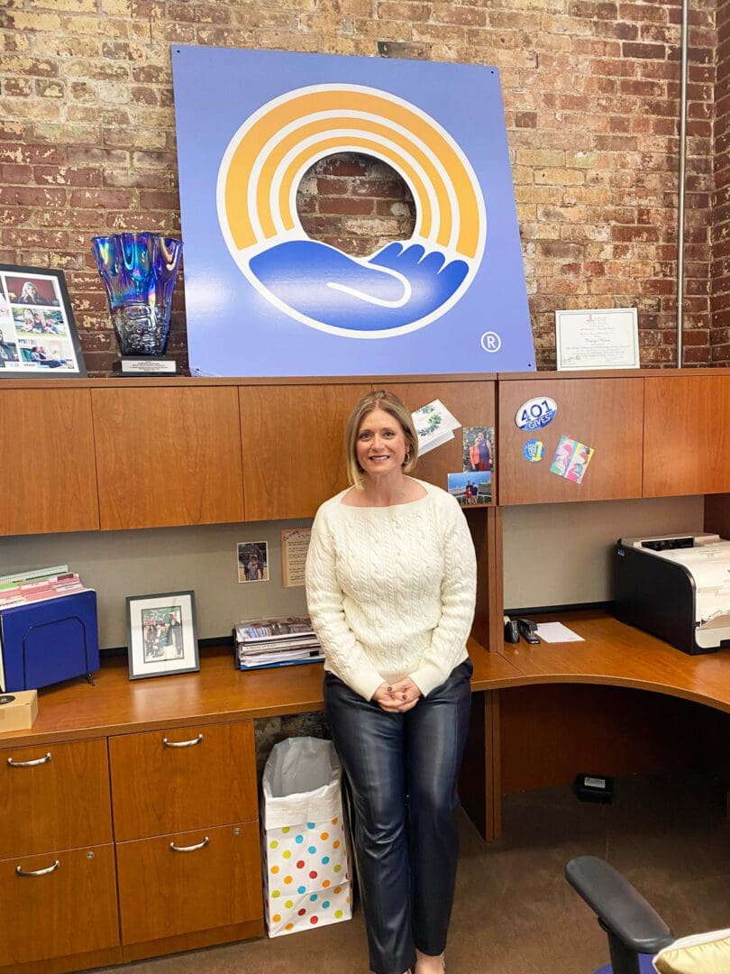 A woman standing in front of a desk with a logo on it.