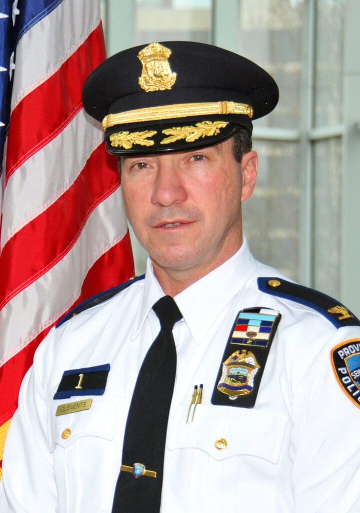 A man in a police uniform standing in front of an american flag.