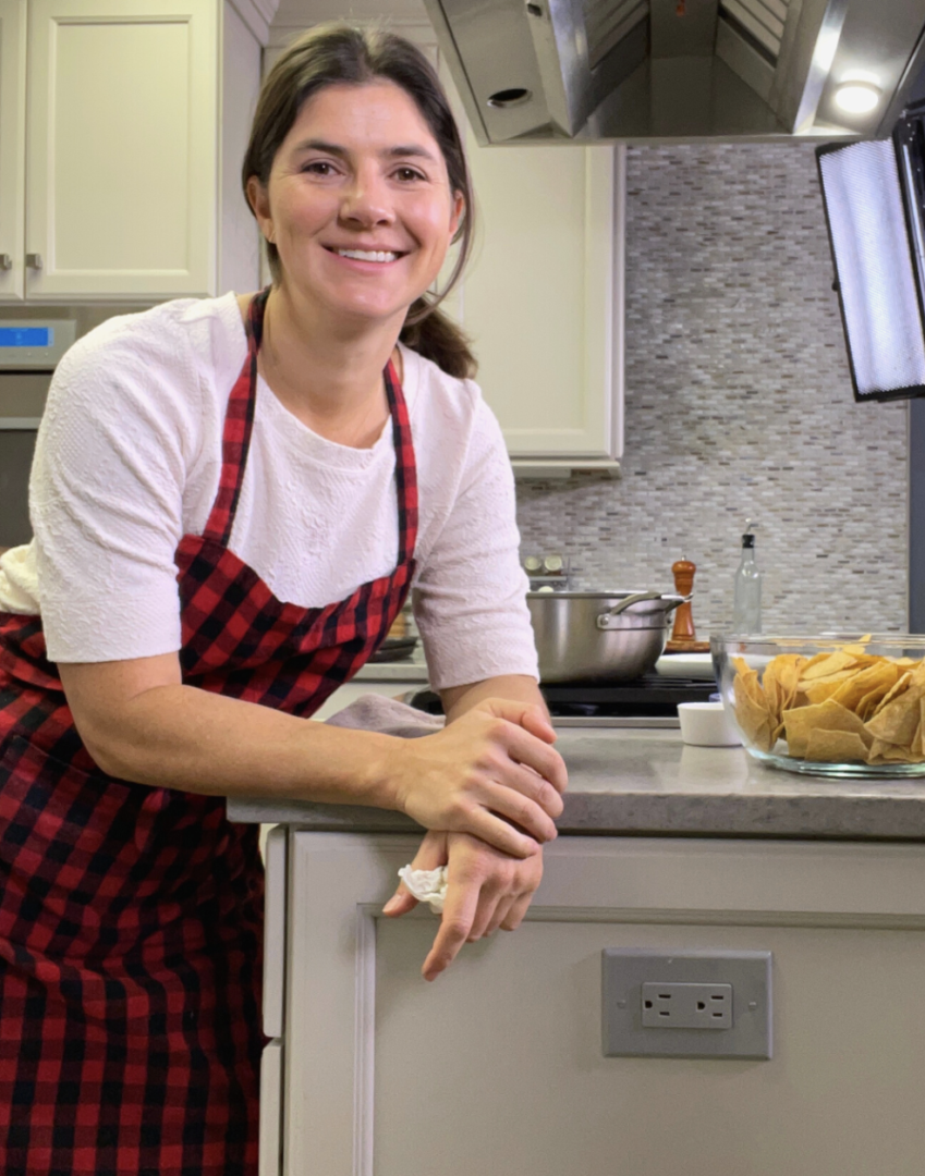 A woman in a red and black apron leaning on a counter.