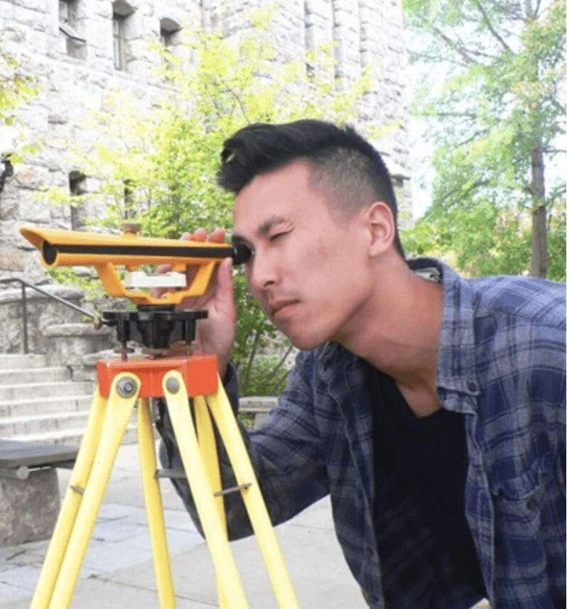 A young man looking at a construction site with a surveyor's tool.