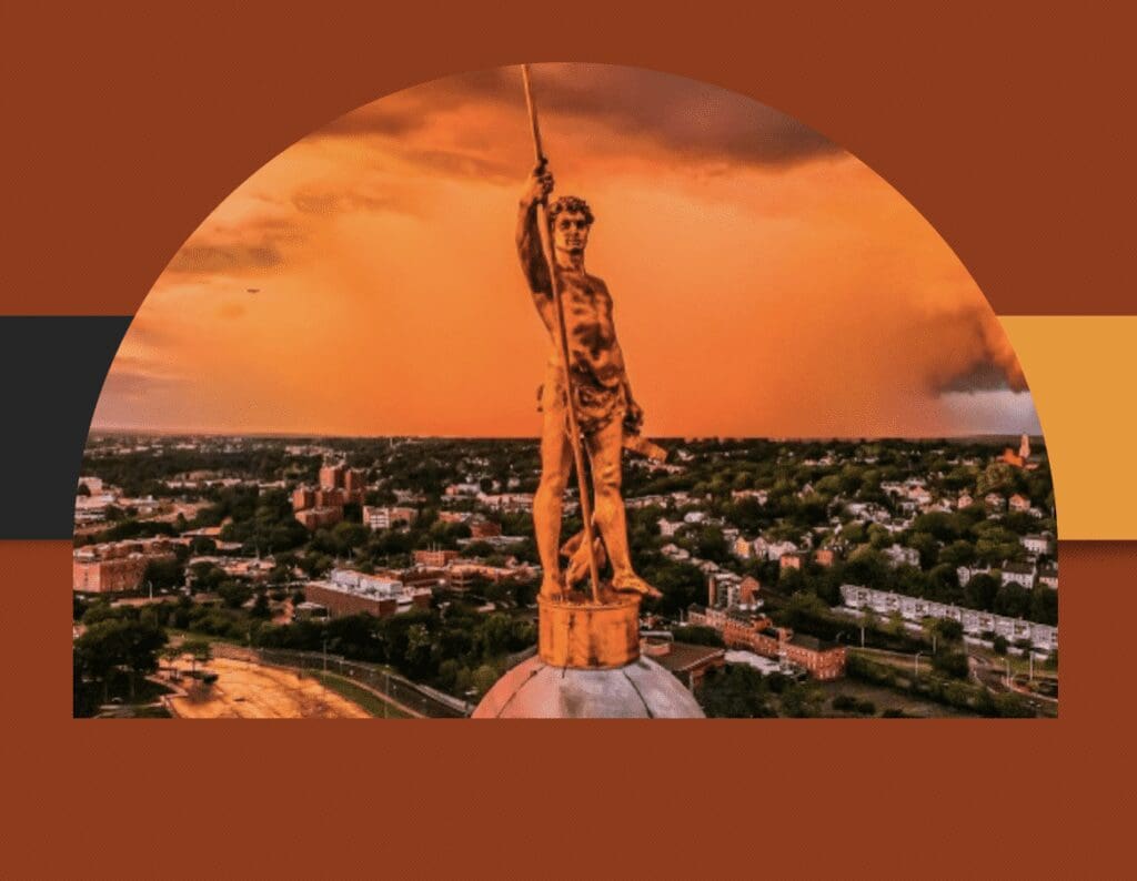 An image of a statue on top of a building with an orange sky.