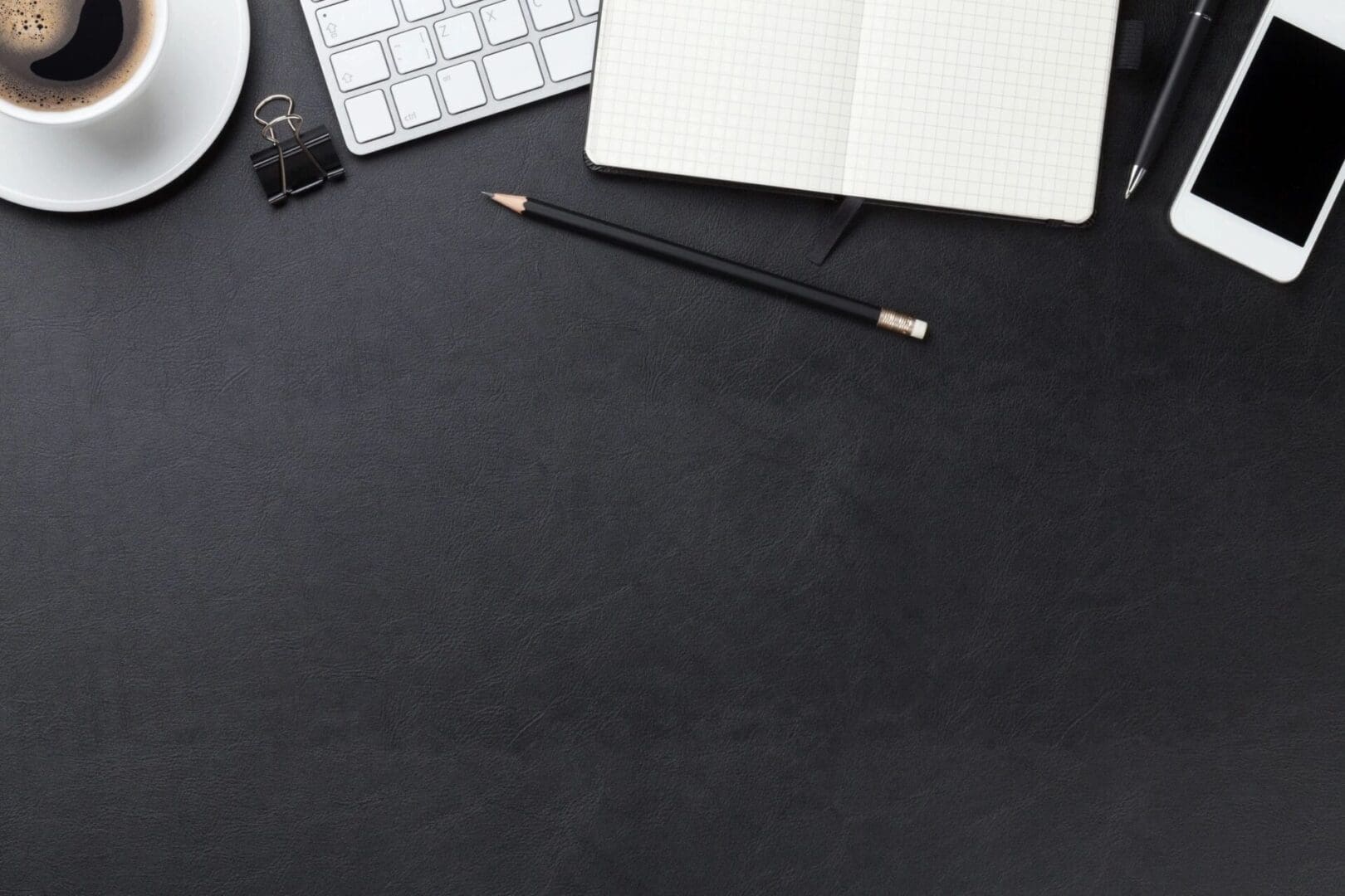 Top view of a black desk with a cup of coffee and a notebook.