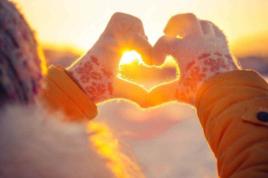 A woman is making a heart shape with her hands in the snow.