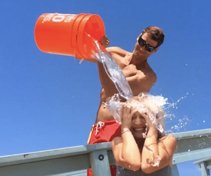 A man is splashing a woman with a bucket of water.
