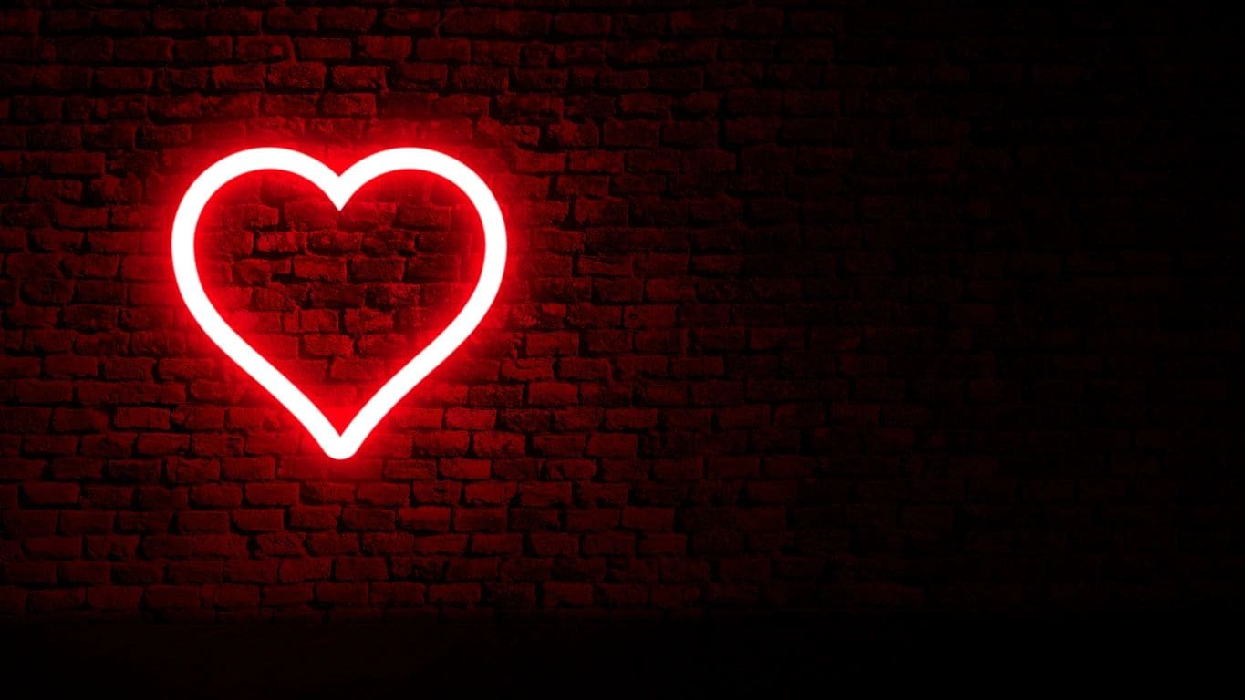 A red heart neon sign on a brick wall.