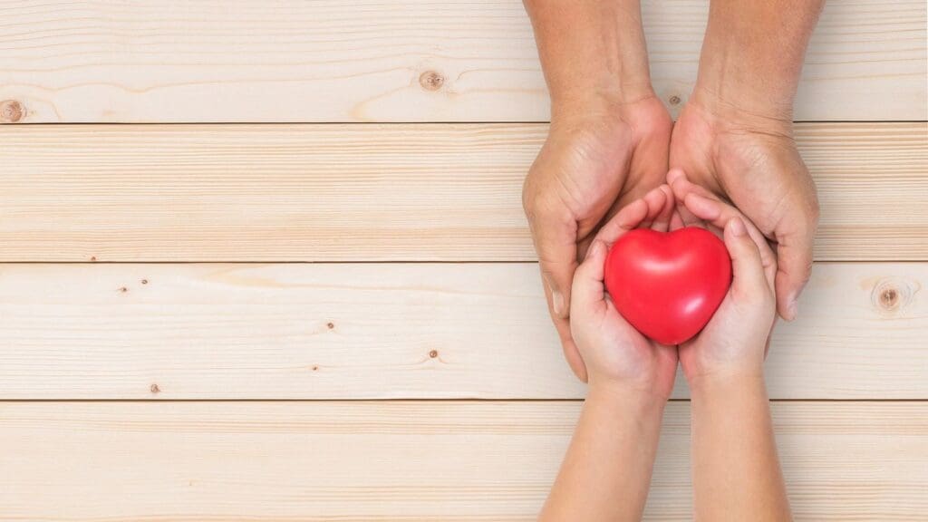 Two hands holding a red heart on a wooden background.