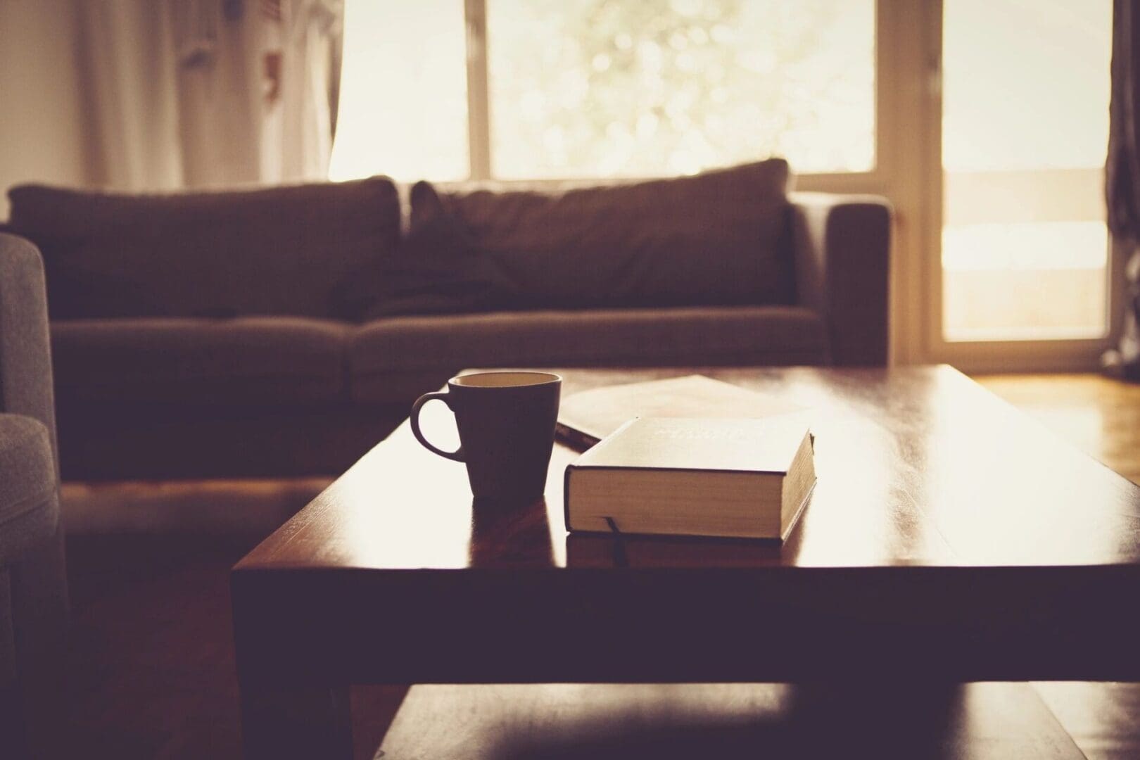 A coffee cup and book on a table in a living room.