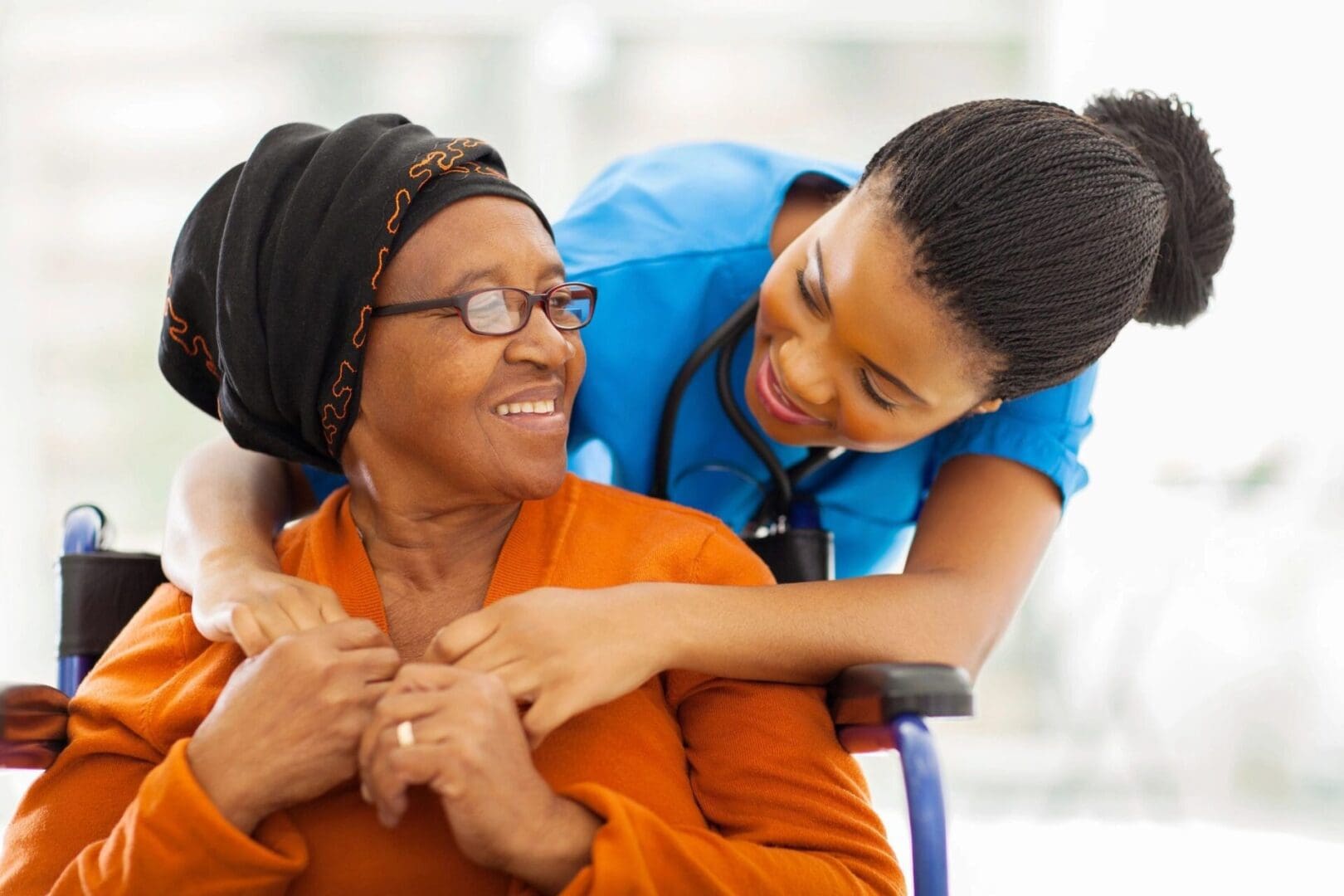 A nurse hugs an elderly woman in a wheelchair.