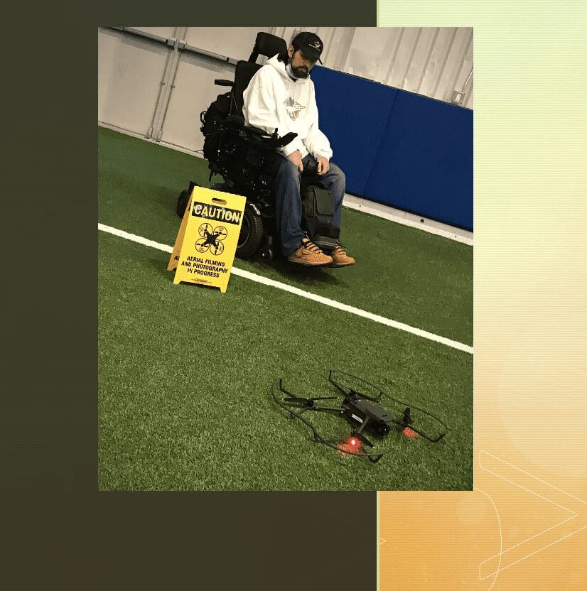 A man in a wheelchair is sitting on a field with a drone.