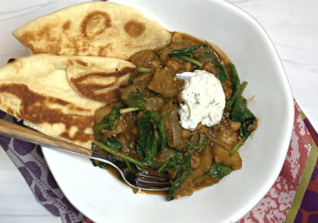 Recipe: A flavorful bowl of spinach curry topped with pita bread and a dollop of sour cream.