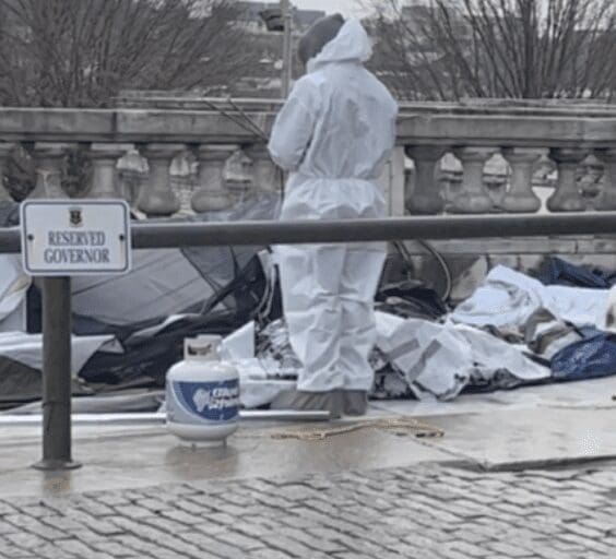 A homeless man in a white suit standing next to a pile of trash in RI.