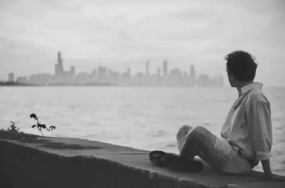 A man sitting on a wall looking at the water with a city skyline in the background, promoting inclusivity and equality.