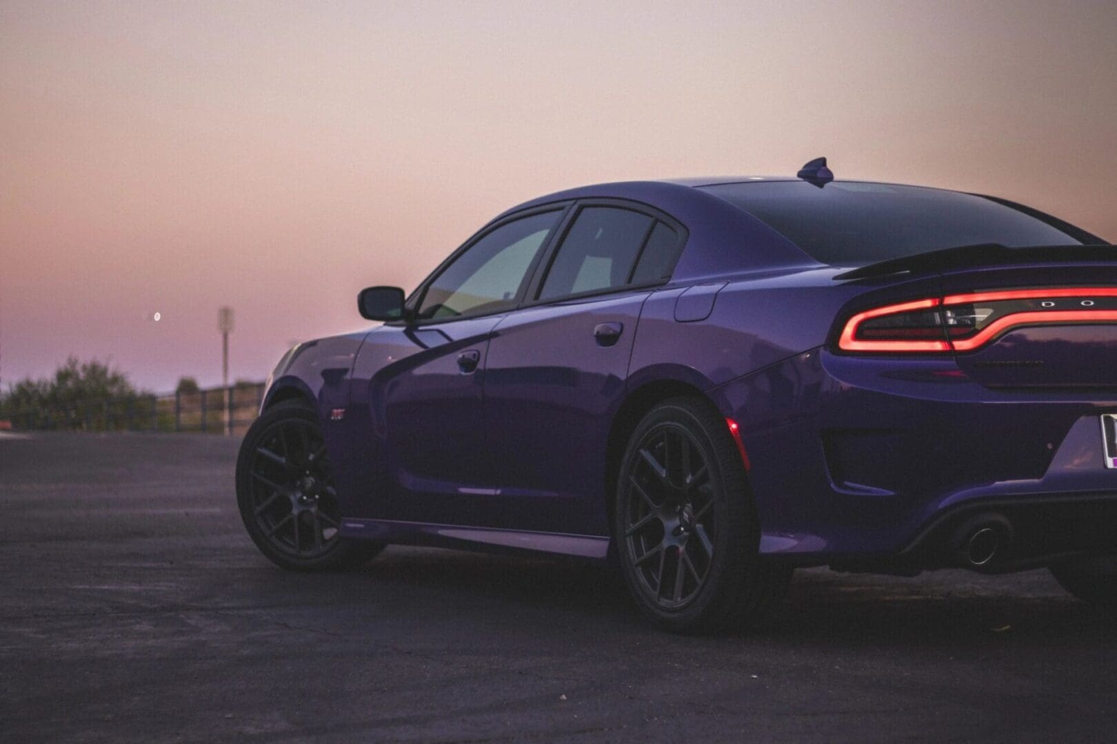 A purple dodge charger parked in a parking lot at sunset.