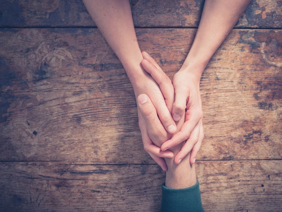 Two people holding hands on a wooden table.