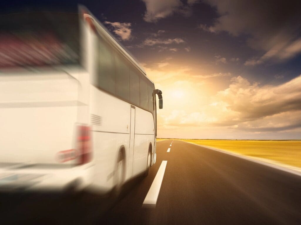 A white bus is driving down the road at sunset.