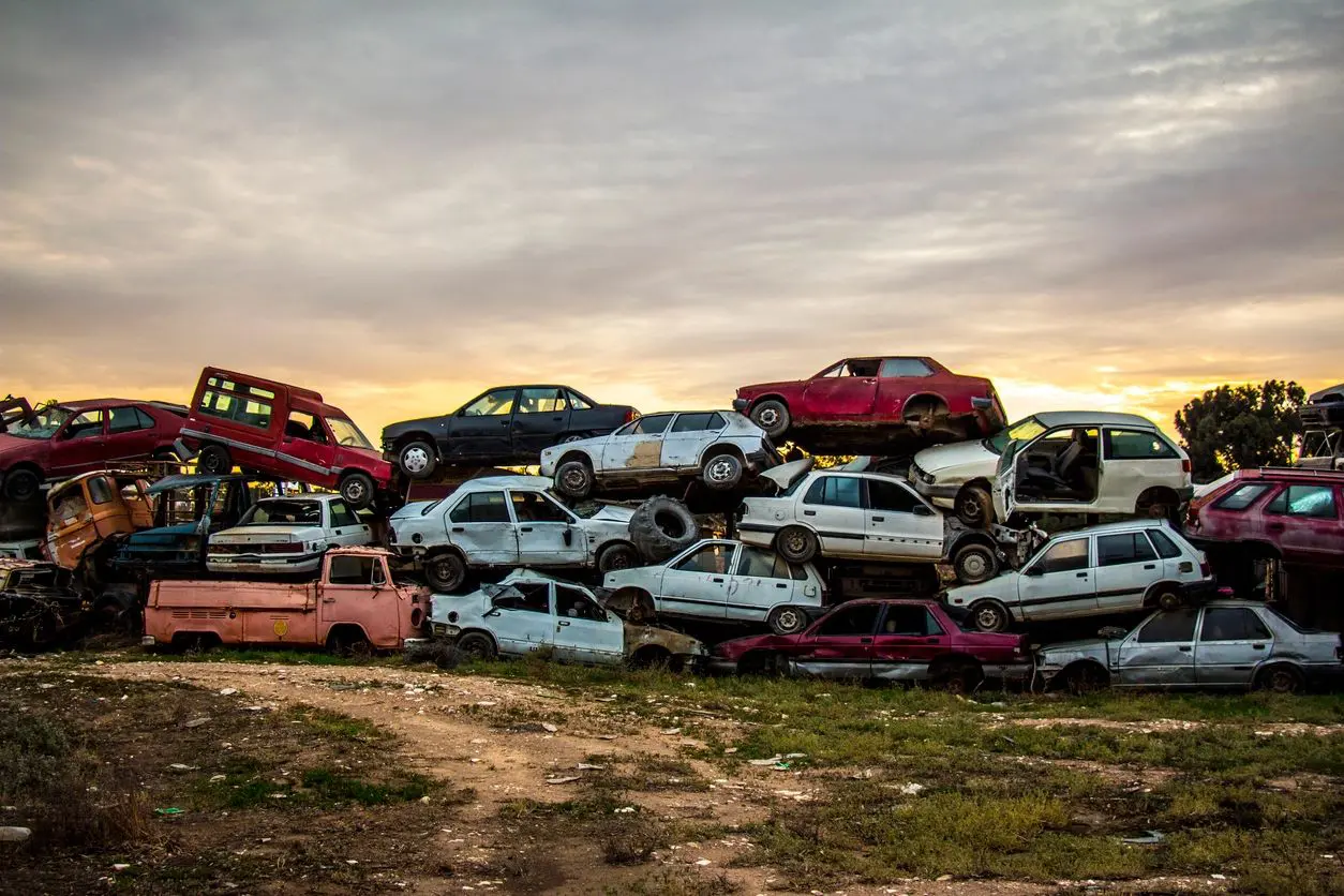 A pile of old cars in a field at sunset.