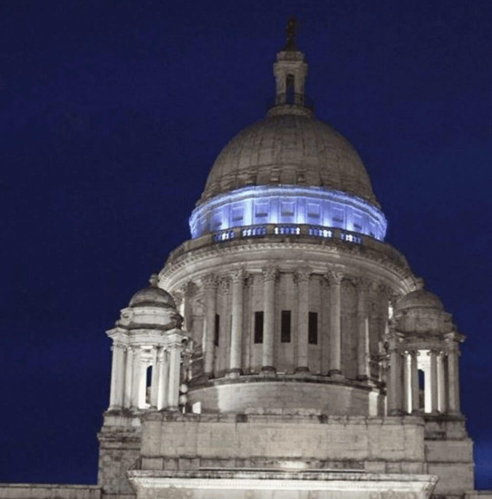 The state capitol building is lit up blue at night, symbolizing legislation.