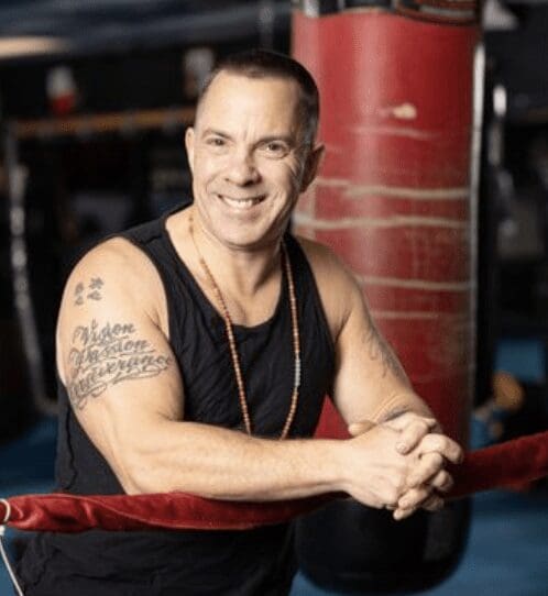 A smiling man with tattoos in a boxing ring.