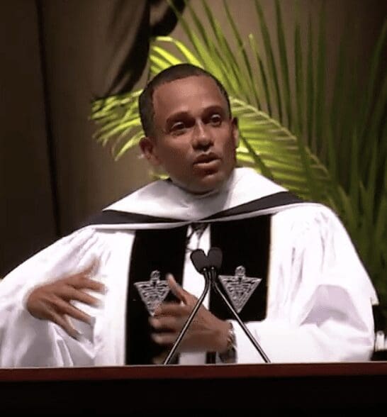 Hill Harper, a man in a robe, speaking into a microphone at Providence College.