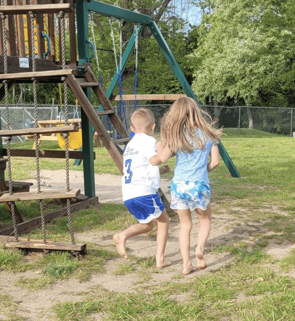 Two children running in front of a playground.