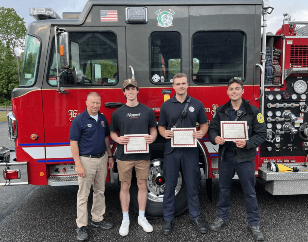 Four firefighters holding certificates in front of a fire truck.