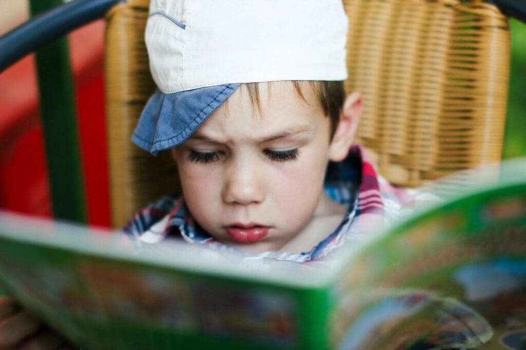 A young boy wearing a hat reading a book.