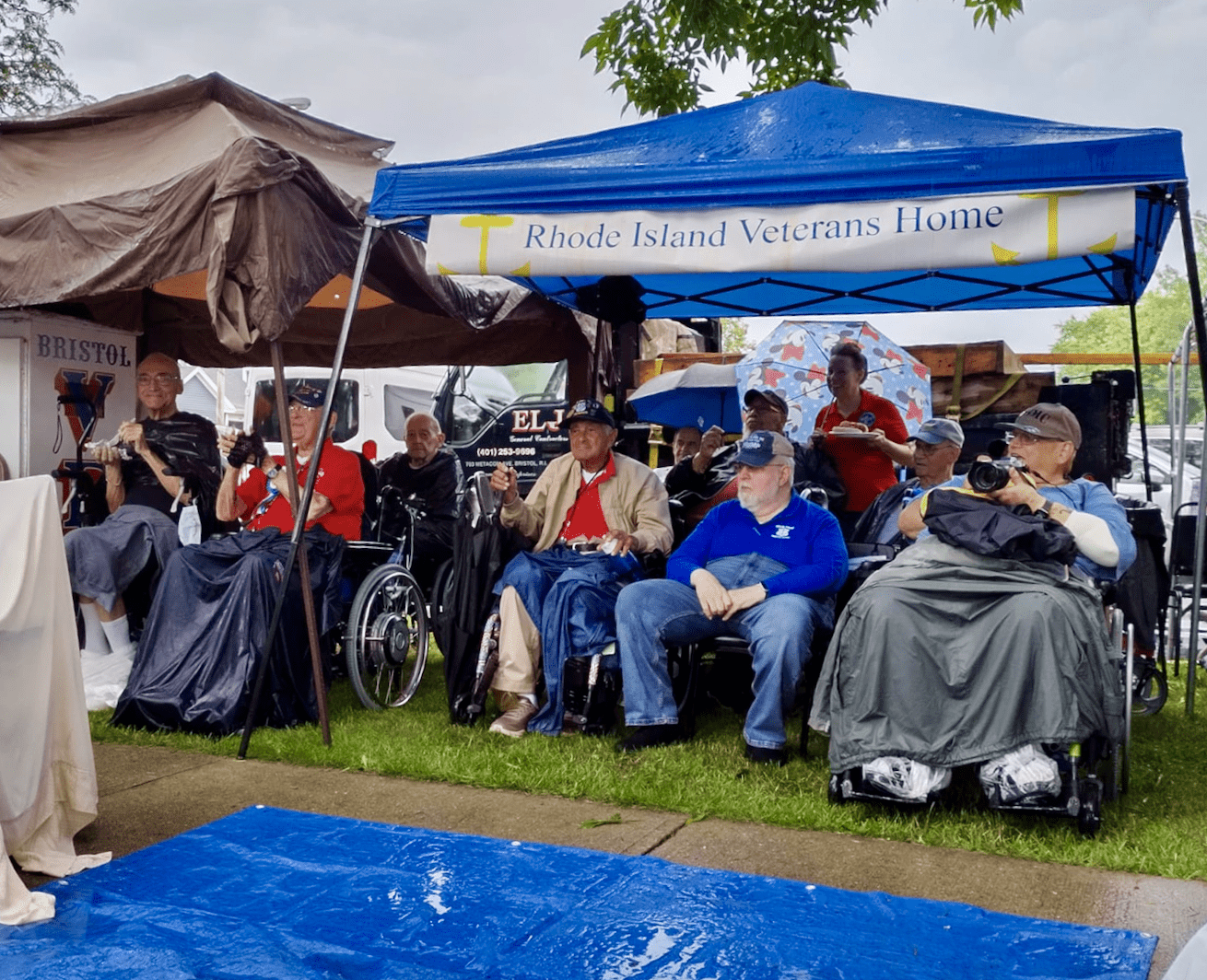A group of veterans in wheelchairs in front of a blue tent.