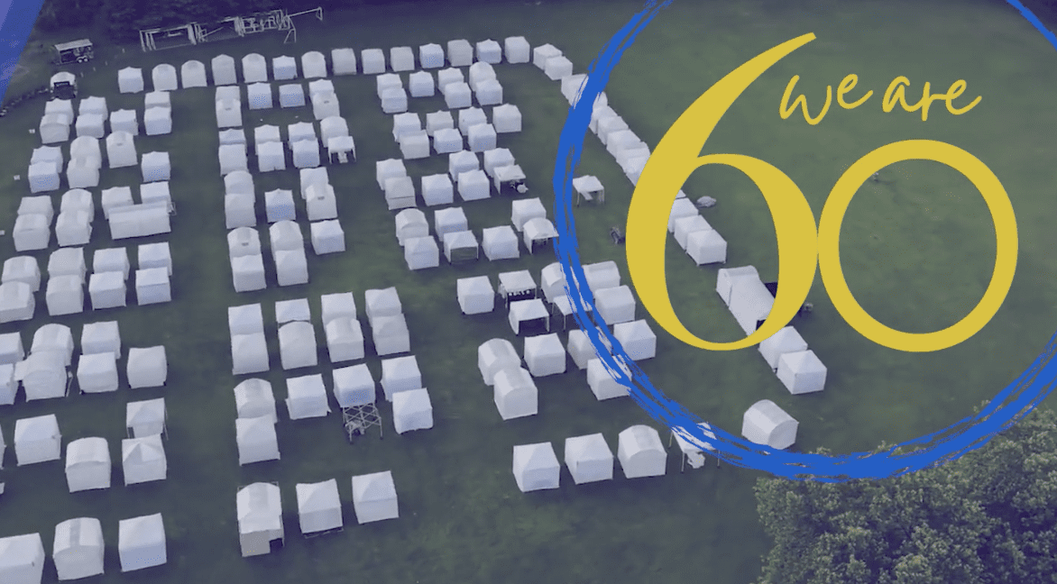 An art festival showcasing a group of tents arranged in a field with the words we're 60.