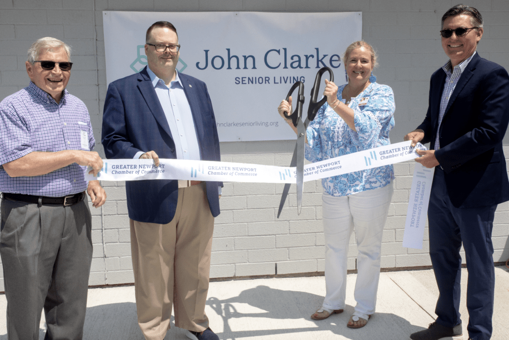 A group of people cutting a ribbon in front of a john clarke sign.