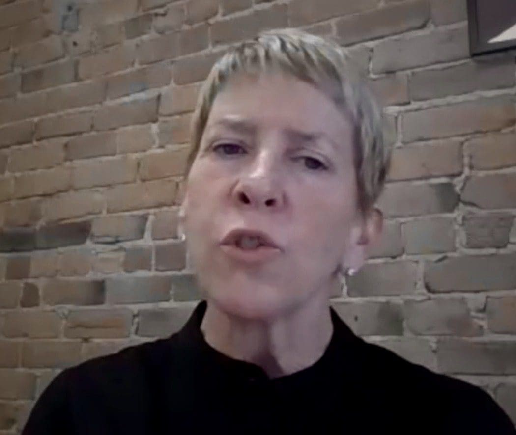 A woman with short hair in front of a brick wall.