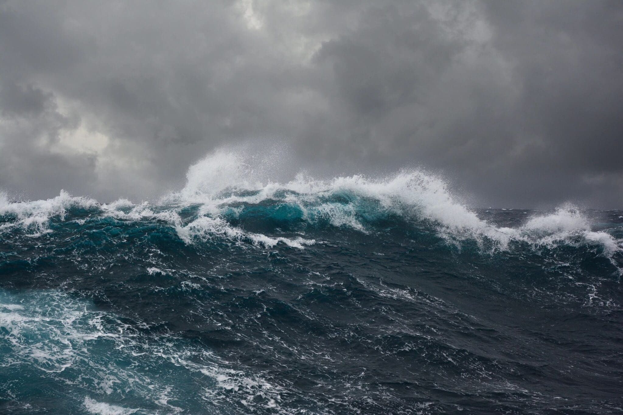 A large wave is crashing in the ocean under a cloudy sky.