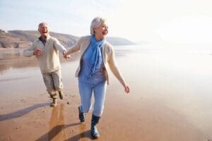 An older couple running on the beach.