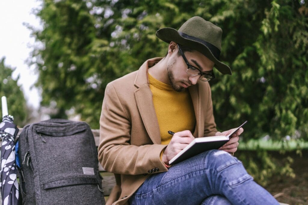 A man in a hat is sitting on a bench and writing in a notebook.