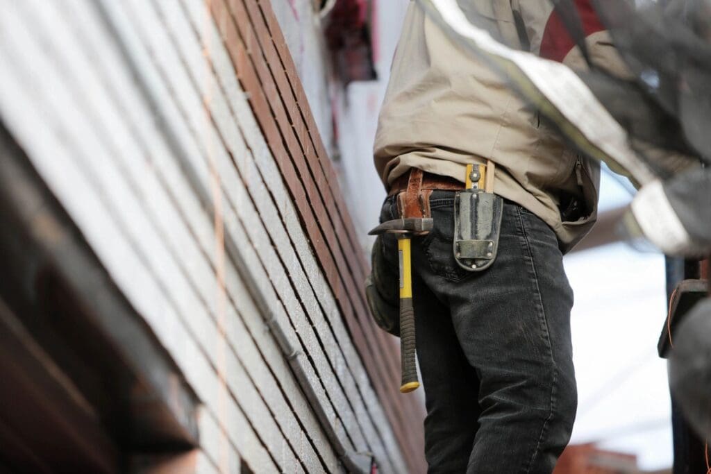 A construction worker is holding a tool on the side of a building.