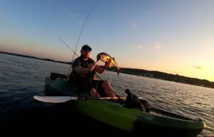 A man holding a fish in a kayak at sunset.