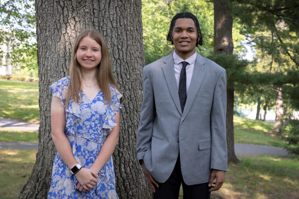Two young people standing in front of a tree.